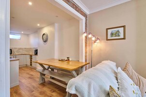 Una habitación acogedora con una mesa de madera, un banco, un sofá blanco, una lámpara de pie, un reloj y un cuadro en la pared.