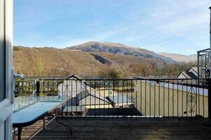 Una terraza con mesa y sillas de vidrio, baranda de metal y vista a una montaña.