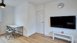 A room with a white door, a TV mounted on the wall, a small white bench, and a table with chairs. - Host Stay Carlisle (Carlisle)