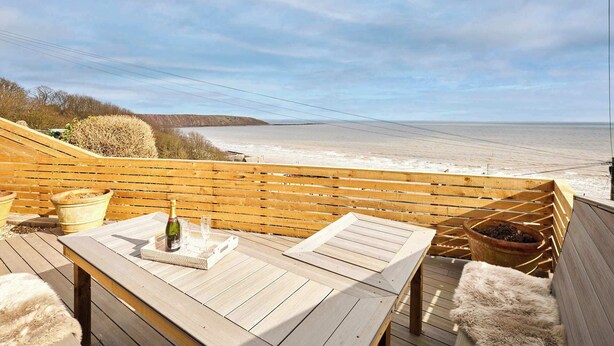 Een houten terras met een tafel en stoelen, met uitzicht op een strand en de oceaan.