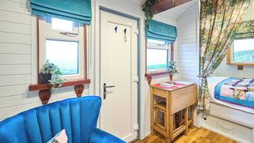 A room with a blue chair, a wooden table, and a bed with floral curtains.