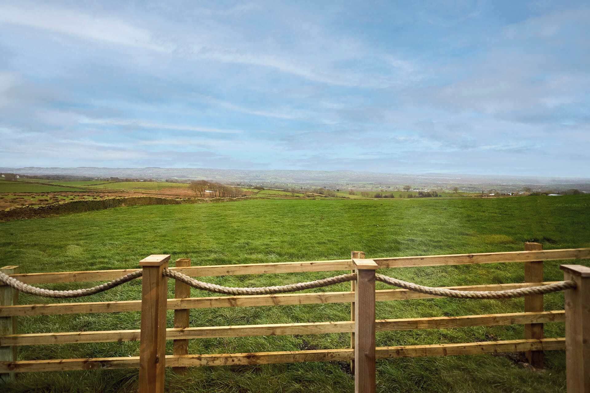 A wooden fence with a rope barrier, a grassy field, and a distant view of a town.