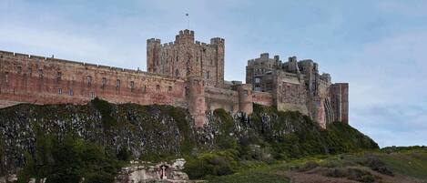 A large castle with multiple towers, situated on a hill with a grassy foreground.