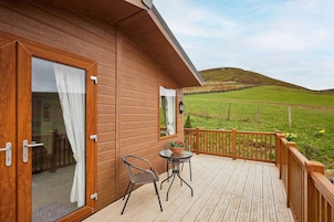 Una cabaña de madera con un balcón, una mesa con sillas y vistas a un campo verde.