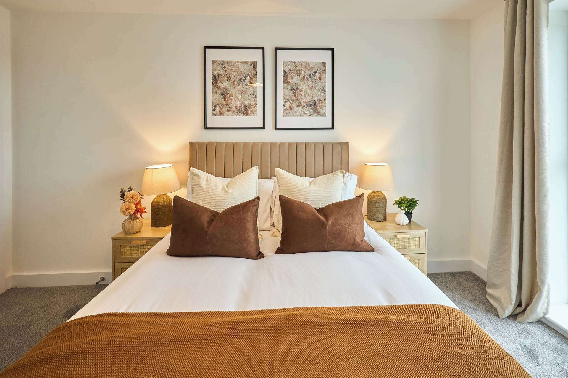 Une chambre d’hôtel avec un lit, deux lampes de chevet, une table de chevet ornée d’un vase de fleurs et deux tableaux encadrés accrochés au mur.