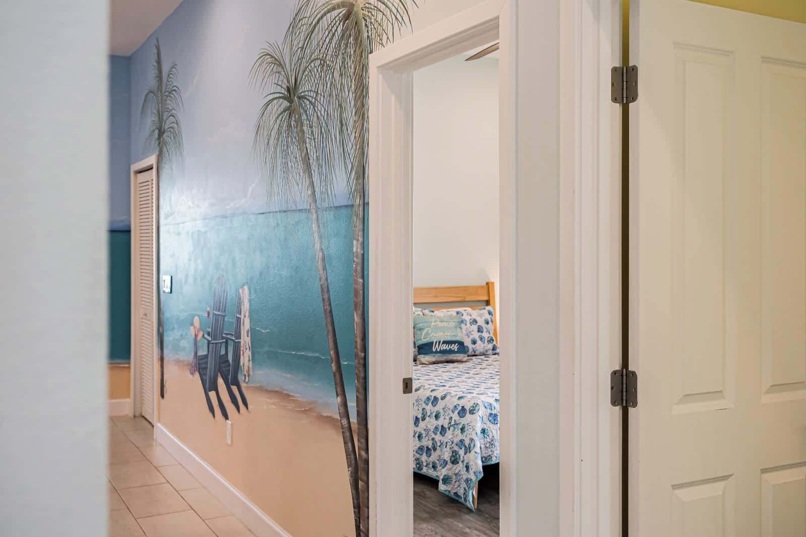 Une chambre avec une fresque murale représentant une plage, un lit recouvert d’une courtepointe à motifs floraux bleus et une porte blanche.