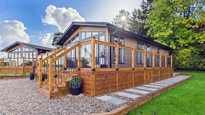 Una cabaña moderna de madera con fachada de vidrio, una terraza de madera y un sendero de grava.