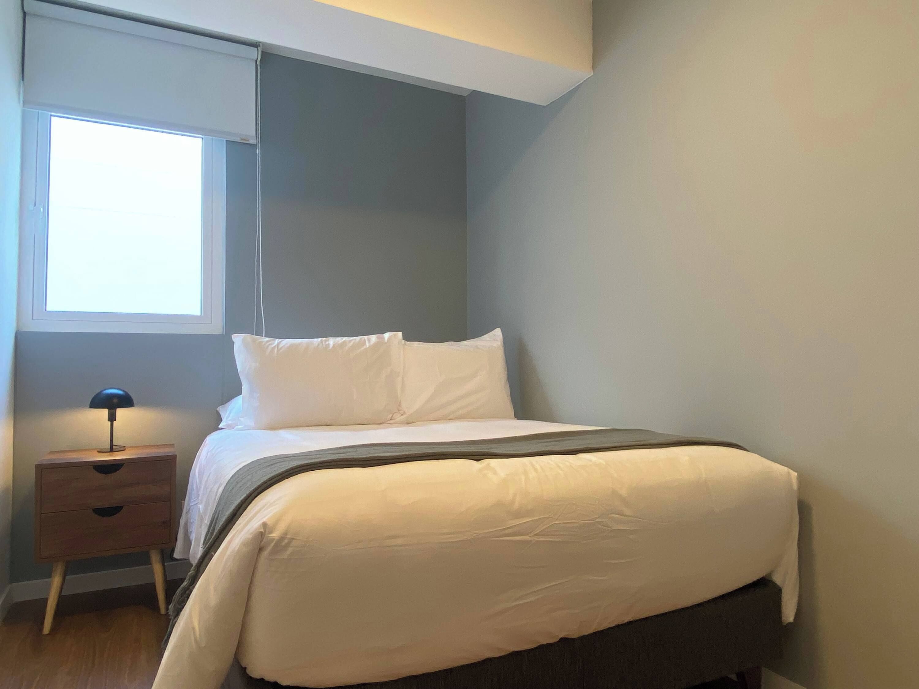 A bedroom with a bed, a nightstand, a lamp, and a window.