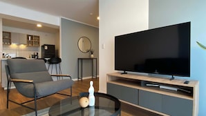 A modern living room with a flat-screen TV, a grey sofa, a glass coffee table, and a kitchen in the background. - w Central 2BR w Balcony in Miraflores (Lima)