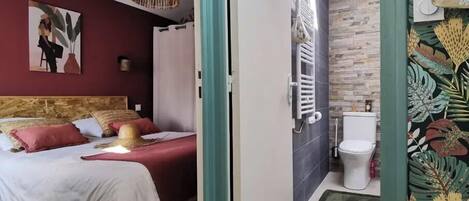 A bedroom with a bed, a bedside table, a hanging light fixture, and a wall-mounted radiator.