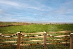 A wooden fence with rope barriers, a grassy field, and a distant view of a town. - Host Stay Curlews Rest (Preston)