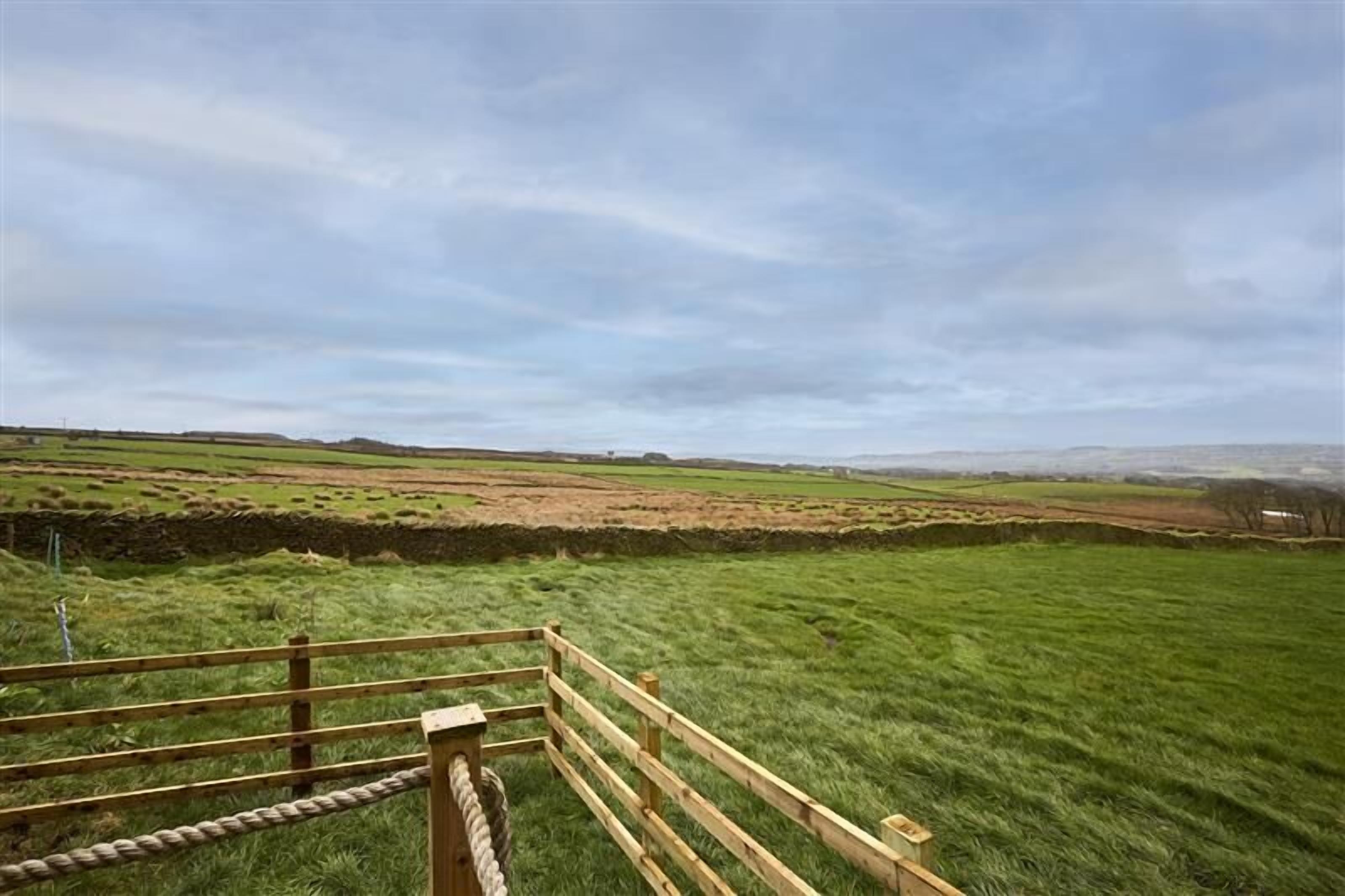 Un paysage rural avec une clôture en bois et un mur de pierres au premier plan, et des collines ondulantes en arrière-plan.