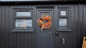 A building with a dark grey exterior, a large door with a decorative wreath, and two windows on either side. - Host Stay Curlews Rest (Preston)