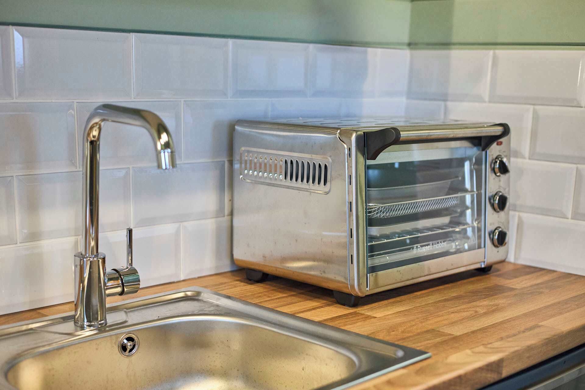 Eine Küche mit Spüle aus Edelstahl, einem modernen Toaster und einer gefliesten Rückwand.