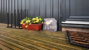 A potted plant with yellow flowers, a stone with a bird illustration, and a wooden bench with a striped pattern. - Host Stay Curlews Rest (Preston)