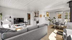 Uma sala de estar moderna com um sofá cinzento, televisão de tela plana e um espaço de refeições com mesa e cadeiras.