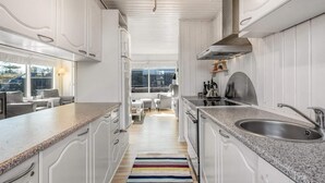 Cozinha moderna com armários brancos, bancadas de granito, pia de aço inoxidável e vista para a sala de jantar.