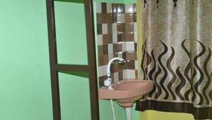 A bathroom with a pink sink, a white faucet, and a patterned curtain.