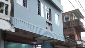 A two-story building with a blue facade, a gated entrance, and a closed shutter on the ground floor.