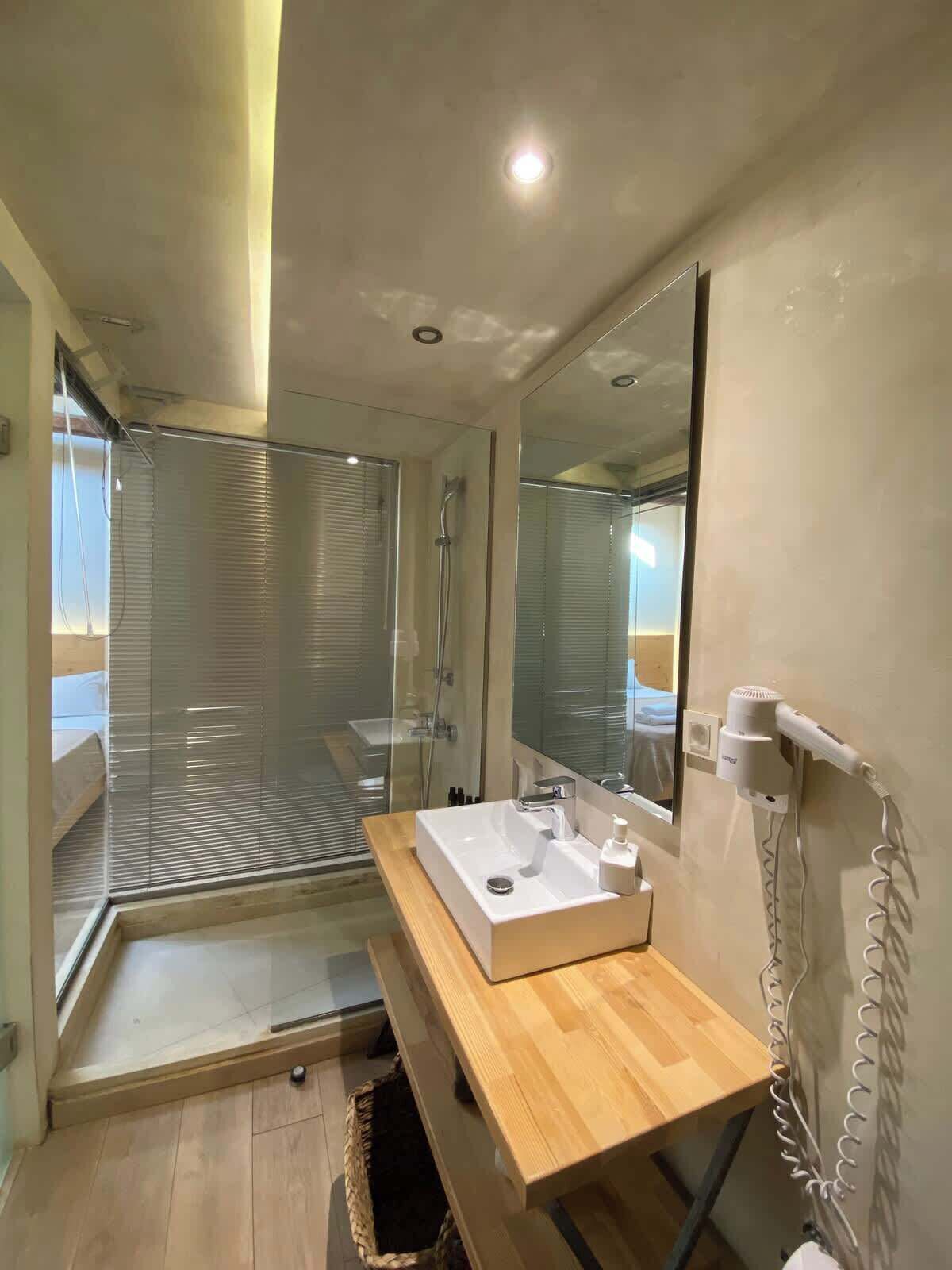 A modern bathroom with a glass shower enclosure, a wooden vanity, a mirror, and a hairdryer mounted on the wall.