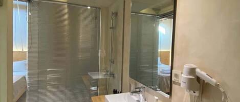 A modern bathroom with a glass shower enclosure, a wooden vanity, a mirror, and a hairdryer mounted on the wall.