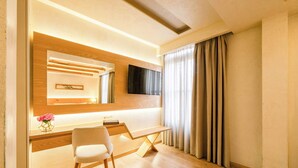 Ein modernes Hotelzimmer mit einem Holztisch, einem Stuhl, einem Flachbildfernseher und einem großen Fenster mit Vorhängen.