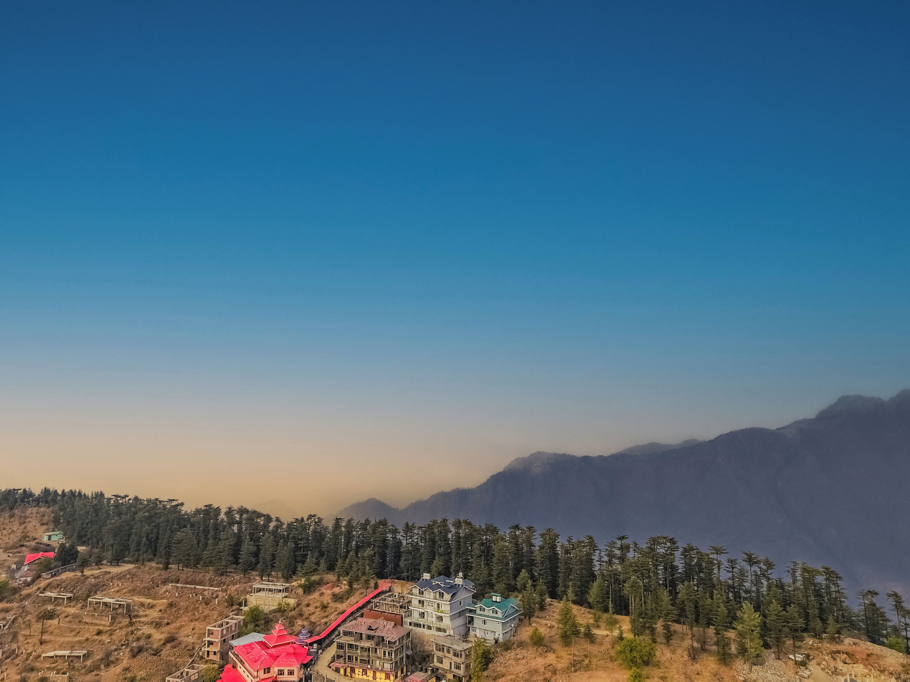 A mountainous landscape with a cluster of buildings, including a prominent red-roofed structure and a larger blue building with a green roof.