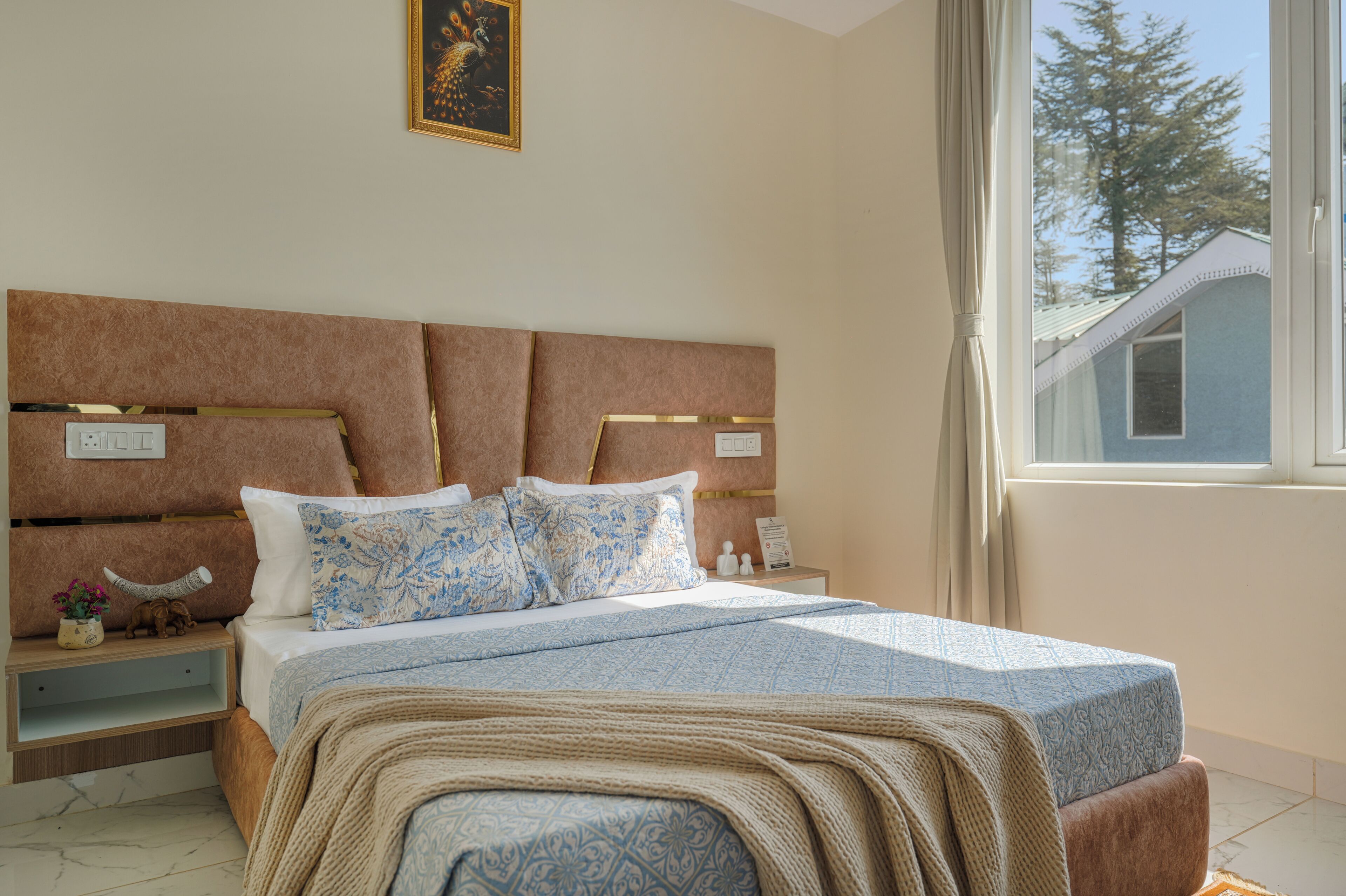 A bedroom with a bed, bedside tables, a nightstand, a window with a view of trees, and a painting on the wall.
