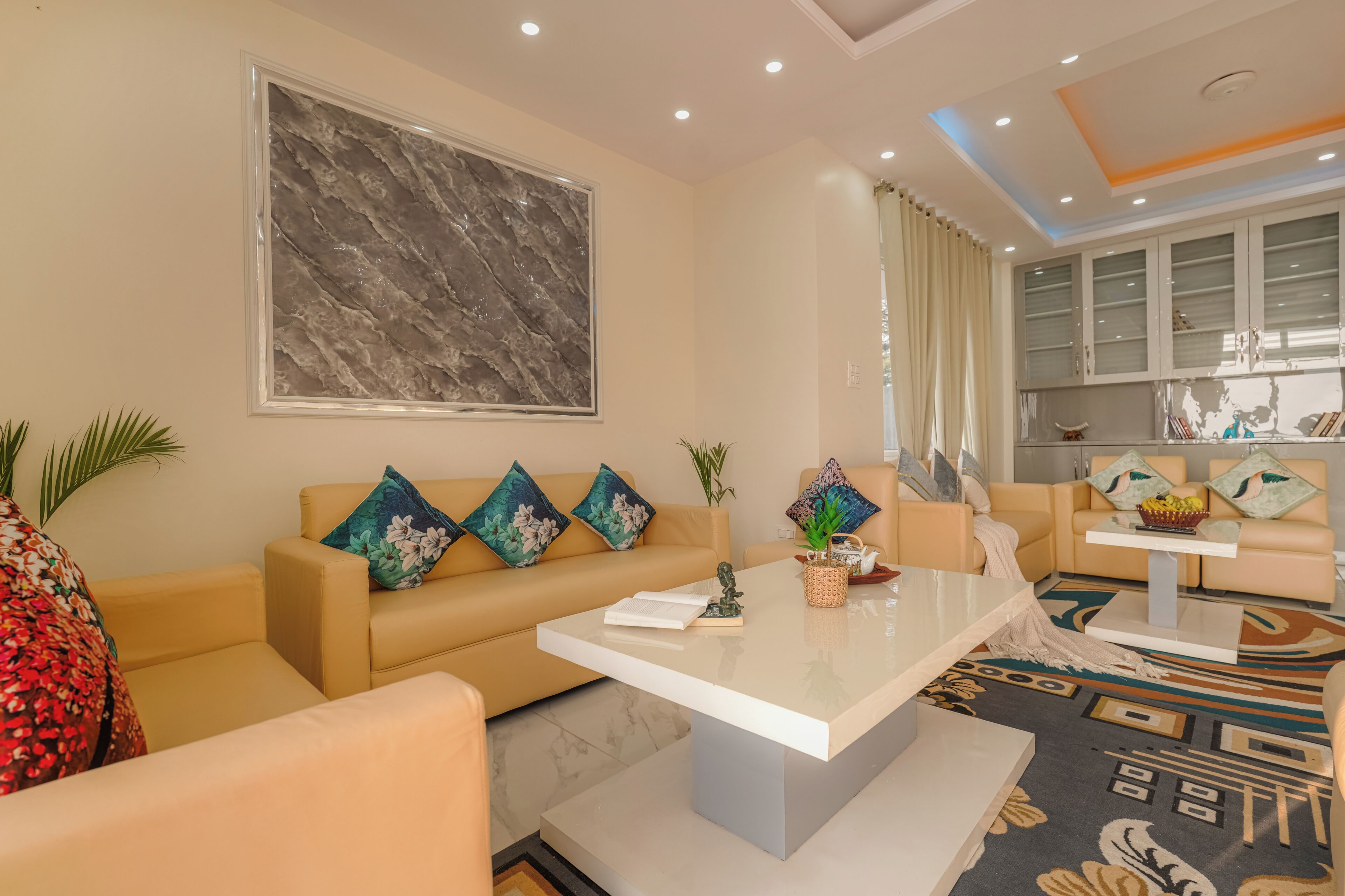 Un salon moderne avec des canapés de couleur beige, une œuvre d’art murale en marbre, une table basse et un tapis à motifs.