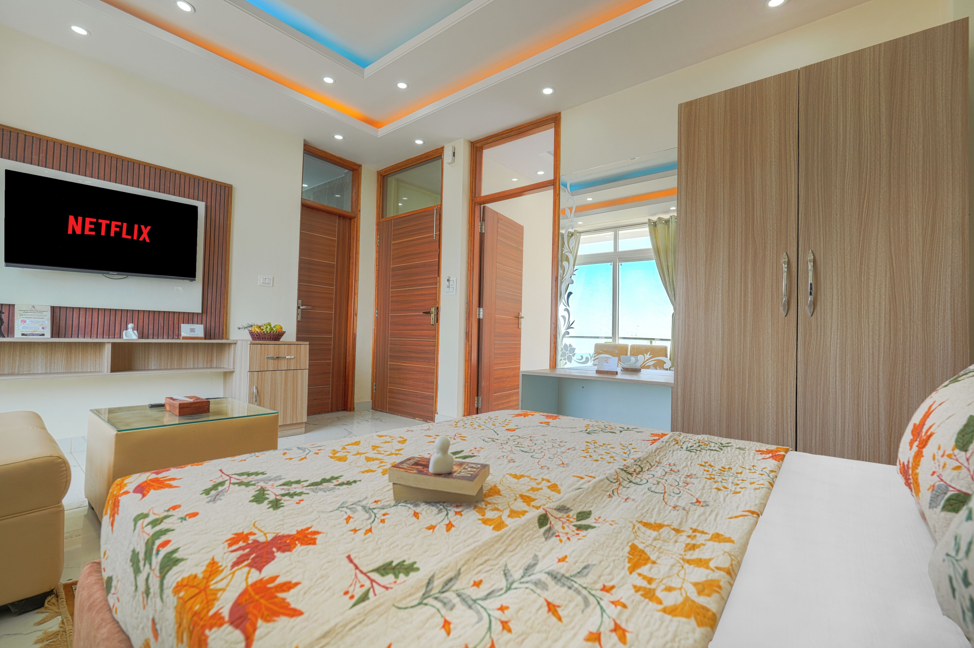 A modern bedroom with a large bed, a TV mounted on the wall, wooden wardrobes, and a window with curtains.