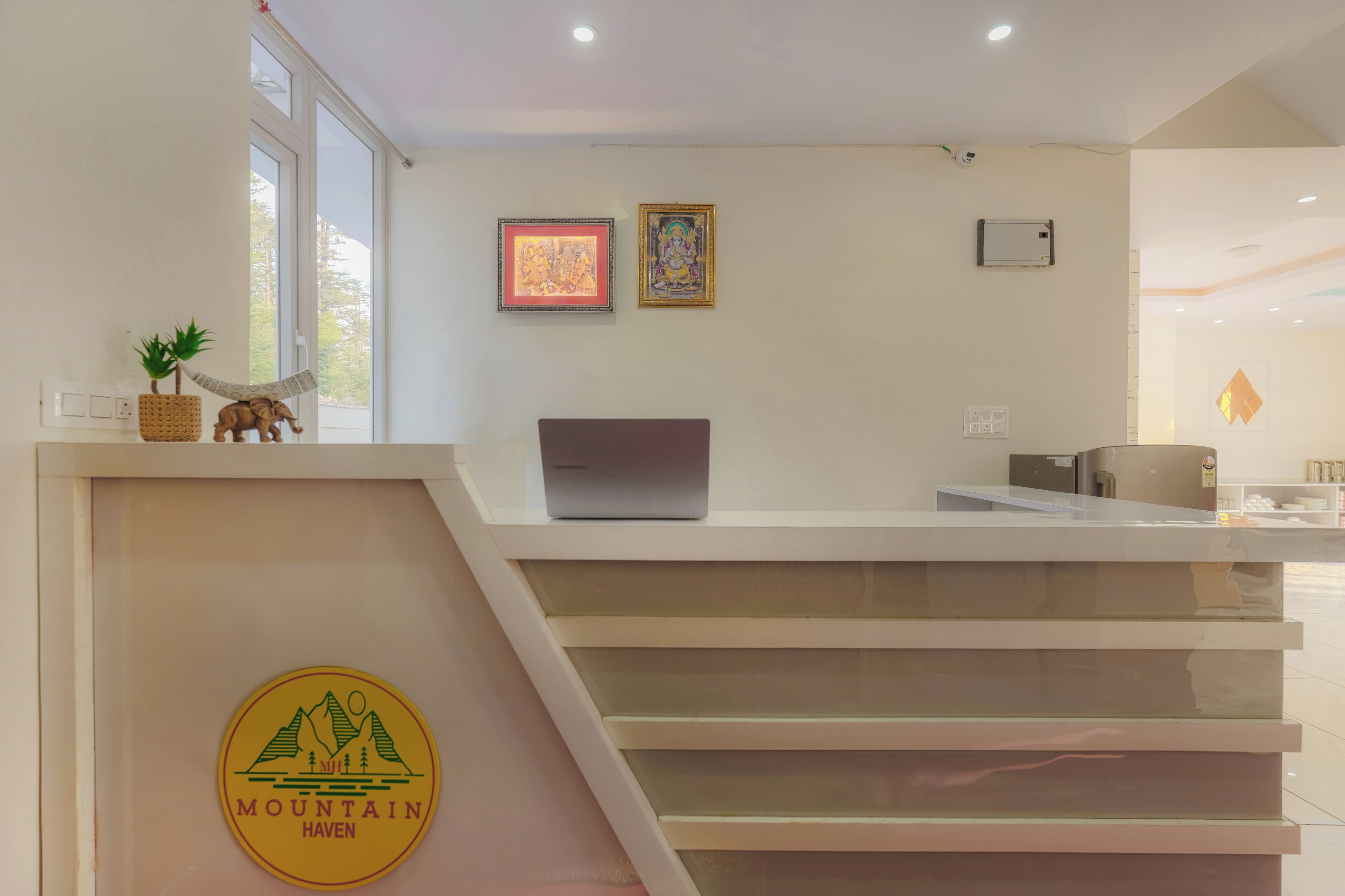 A reception desk with a laptop, framed artwork, and a logo on the wall.
