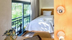 A hotel room with a bed, a desk with a lamp, a window with curtains, and a view of greenery outside. - Panellinion Single Getaway - Seaescape by the Port (Kalamata)