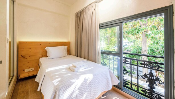 A bedroom with a wooden headboard, a large window with a view of greenery, and a neatly made bed with a white duvet. - Panellinion Single Getaway - Seaescape by the Port (Kalamata)