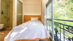 A bedroom with a wooden headboard, a large window with a view of greenery, and a shower area. - Panellinion Single Getaway - Seaescape by the Port (Kalamata)