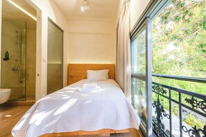 Ein Schlafzimmer mit Holzkopfteil, einem großen Fenster mit Blick auf Grünflächen und einer Duschkabine.