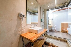 Ein modernes Badezimmer mit einem Holzkonsolenunterschrank, einem großen Spiegel, einem weißen Waschbecken, einem Haartrockner und einer Duschkabine aus Glas.