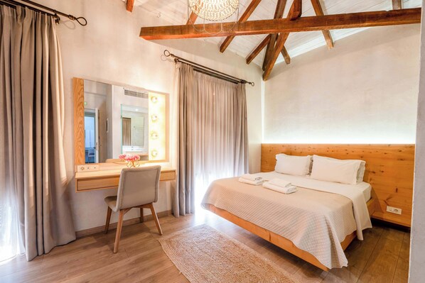 A bedroom with a wooden bed, a desk with a chair, a mirror, and curtains. - Panellinion Beachfront Gem - Cozy Seaside Loft (Kalamata)