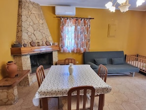 Ein Essbereich mit Kamin aus Stein, einem Tisch mit Blumenmuster-Tischdecke und einer Couch.