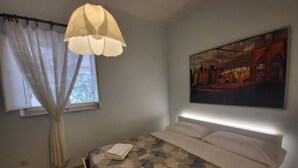 A bedroom with a bed, a window with curtains, a hanging light fixture, and a wall-mounted painting. - Villa Isabella Guest House - with Garden, Parking and WiFi (Ostuni)