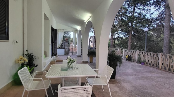 Eine überdachte Terrasse mit Tisch und Stühlen und einem Blick auf die Umgebung, sowie ein Geländer.