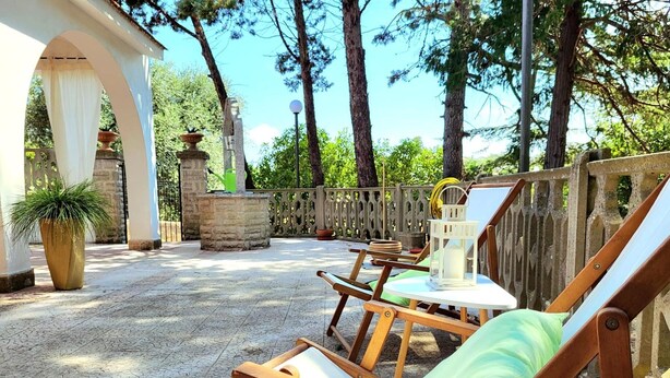 A patio with wooden lounge chairs, a table, and a potted plant. - Villa Isabella Guest House - with Garden, Parking and WiFi (Ostuni)