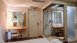 A hotel room with a bed, a desk with a chair, a mirror, a shower area, and a door. - Panellinion Beachfront Gem, Comfy Double Sea Nest (Kalamata)