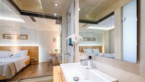 A modern hotel room with a large mirror, a wooden bed, a glass shower enclosure, and a white sink. - Panellinion Beachfront Gem, Comfy Double Sea Nest (Kalamata)