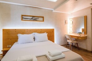 Quarto com cabeceira de madeira, cama com roupa de cama branca, escrivaninha com espelho e luminária fixada na parede.