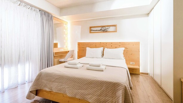 A bedroom with a wooden bed, white linens, a bedside table, a mirror with lights, and a framed picture on the wall. - Panellinion Beachfront Gem, Comfy & Sunny Triple (Kalamata)