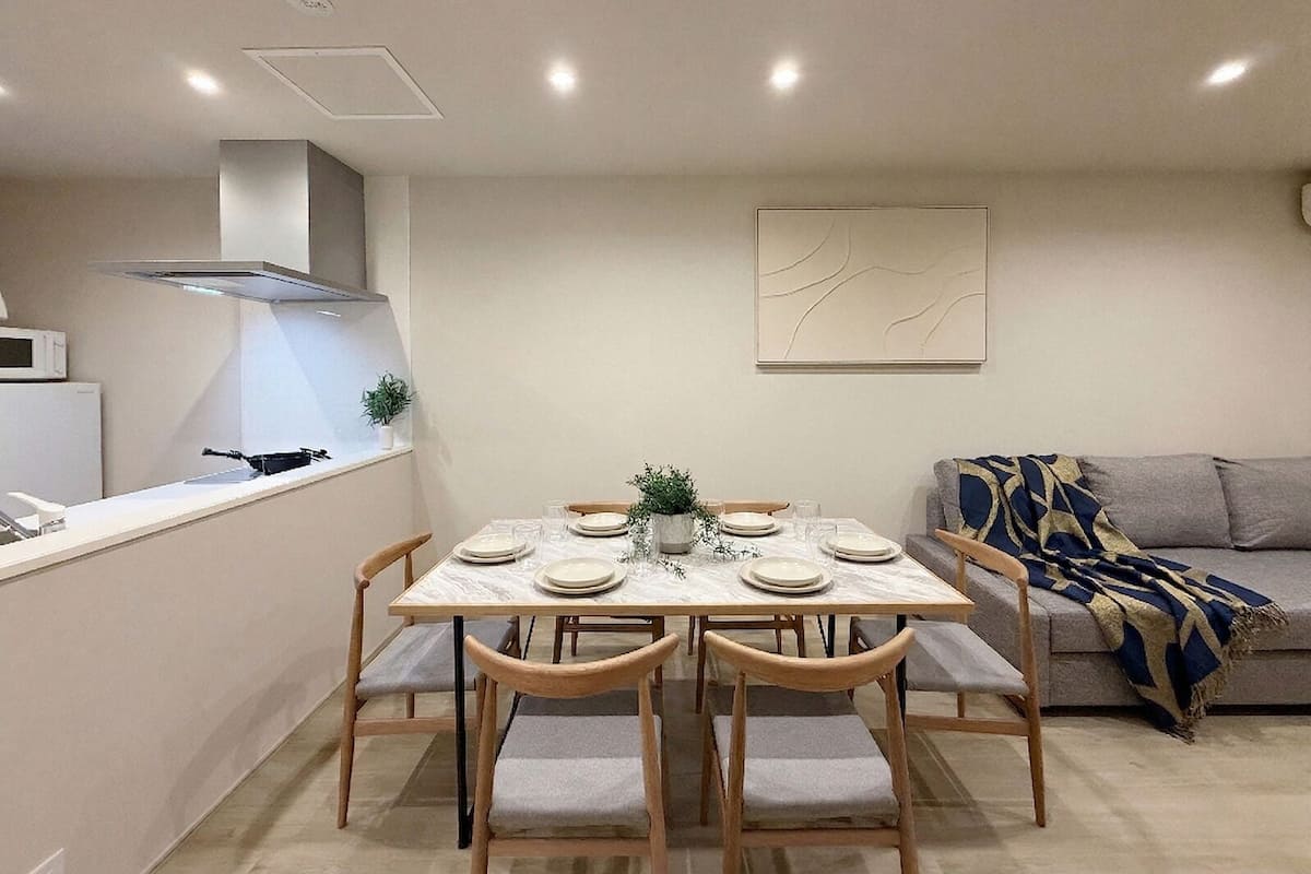 A dining area with a marble table, wooden chairs, a microwave, and a sofa with a patterned throw.