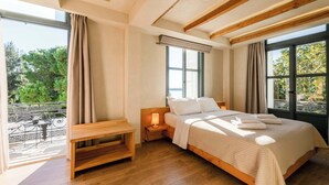 A bedroom with a wooden bed, a nightstand with a lamp, a bench, and large windows offering a view of greenery. - Panellinion Beachfront Getaway - Sea Sunny Gem (Kalamata)