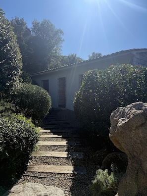 A stone staircase leading to a building with a tiled roof, surrounded by greenery and a large rock. - Quiet Lucia sheepfold, private heated pool (Figari)