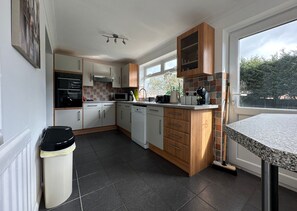 A modern kitchen with white cabinets, a dishwasher, a microwave, and a coffee machine. There is a window providing natural light and a view of trees outside. - Spacious 5 Bedroom With 4 Baths Off-road Parking (Peterborough)
