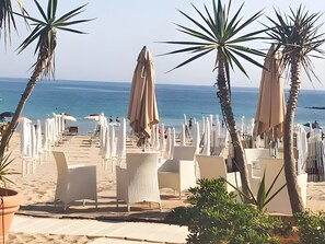 Un cadre idyllique au bord de la plage, avec des chaises longues blanches et des parasols, des palmiers et une vue sur la mer.